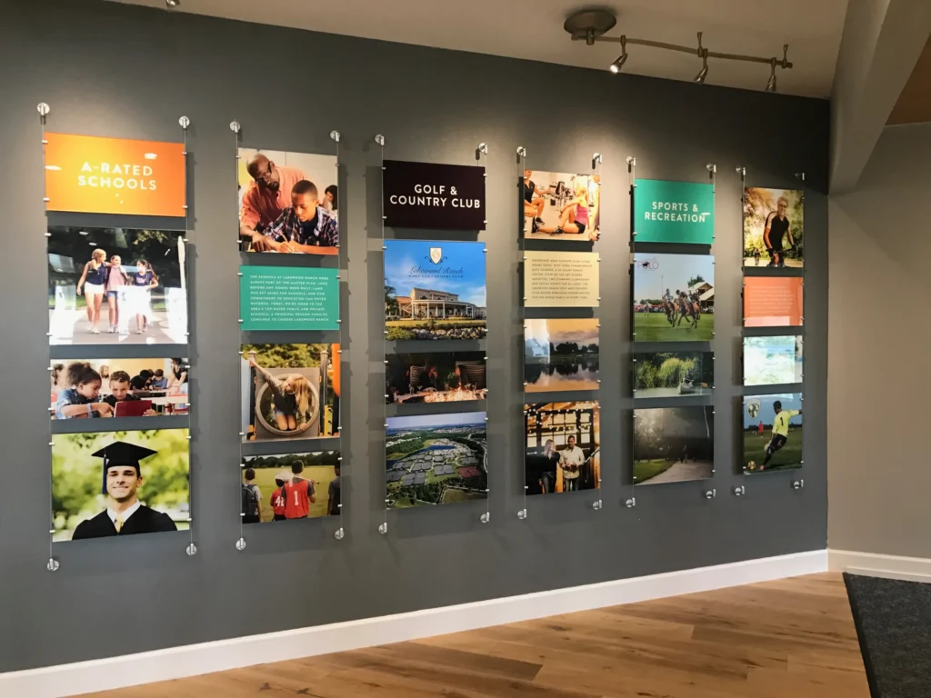 A wall display with panels showing images and text about schools, a golf club, and sports and recreation, mounted on a gray wall with wooden flooring below.