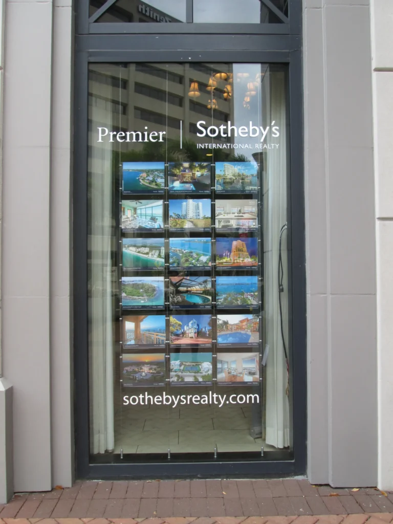 A Premier Sotheby’s International Realty office window displays property listings and the company website, sothebysrealty.com.