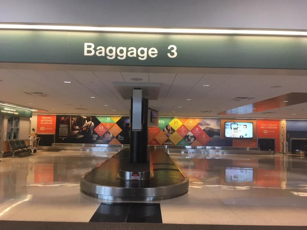 Baggage claim area 3 in an airport, with a luggage carousel, informational signs, and colorful wall displays in the background.