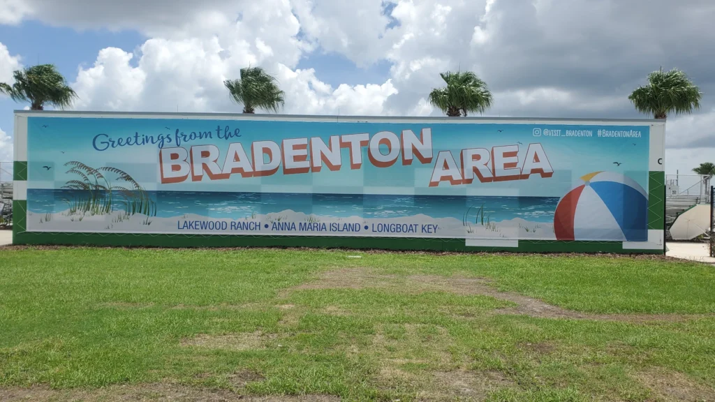 Large mural reads “Greetings from the Bradenton Area” with beach scenery, palm trees, and a beach ball; mentions Lakewood Ranch, Anna Maria Island, and Longboat Key below.
