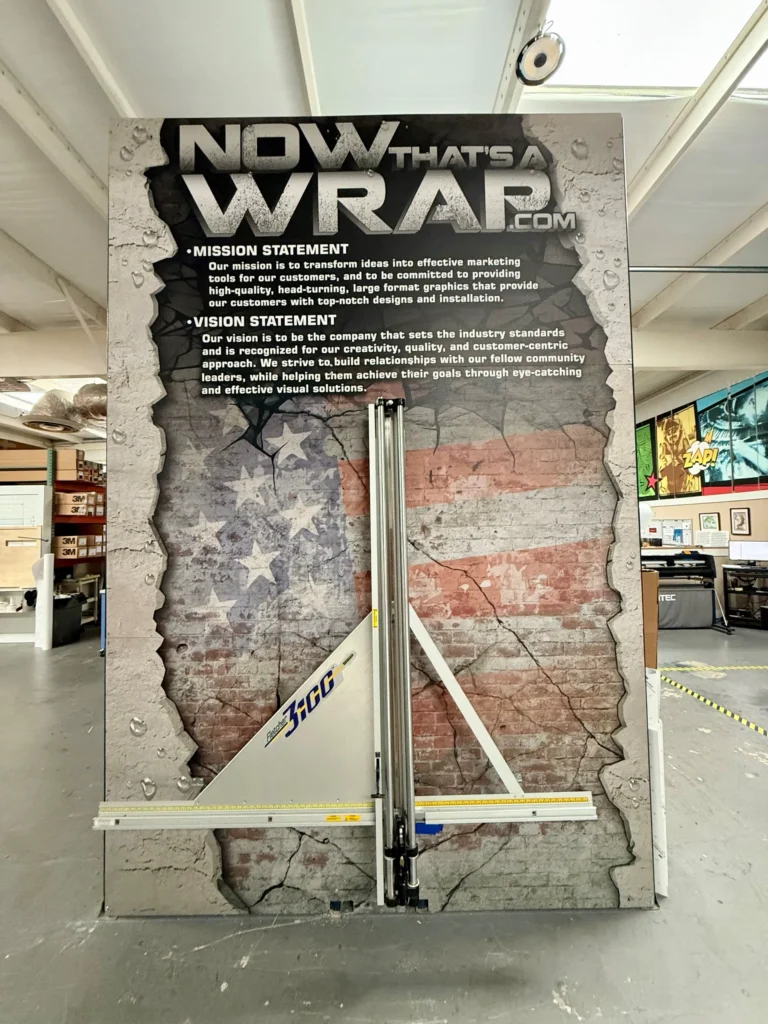 A large wall display with a faded American flag, featuring the company name “Now That’s a Wrap” and its mission and vision statements in white text.