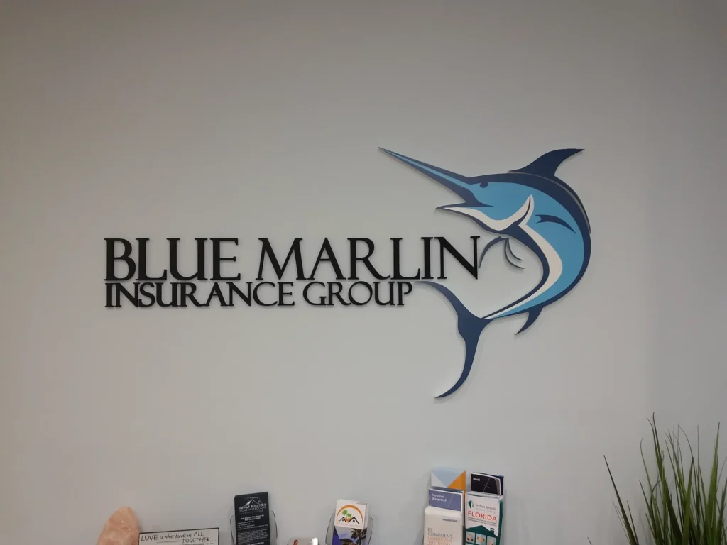 Wall sign with the text “Blue Marlin Insurance Group” next to a stylized blue marlin fish logo; brochures are displayed on a countertop below.