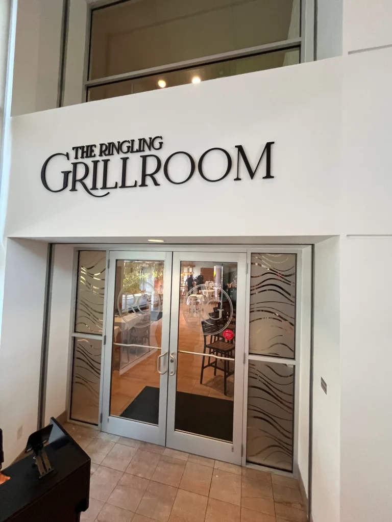 Entrance to The Ringling Grillroom, featuring glass double doors with decorative wave patterns and a large sign above the entrance.