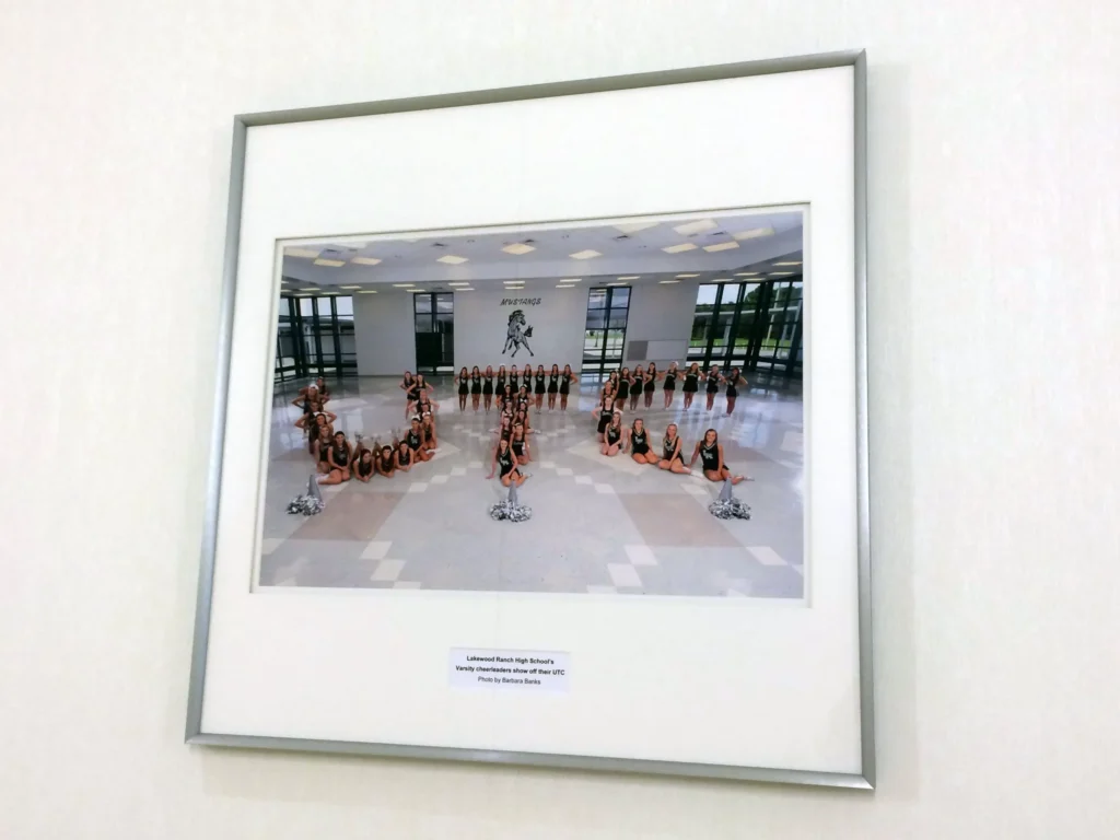 Framed photo of a cheerleading team posing in a lobby, forming the letters “UCF” with their bodies and pom-poms.