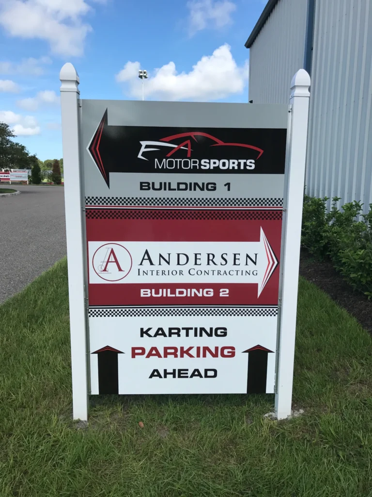 Outdoor sign showing directions to FA Motorsports Building 1, Andersen Interior Contracting Building 2, and karting parking ahead.