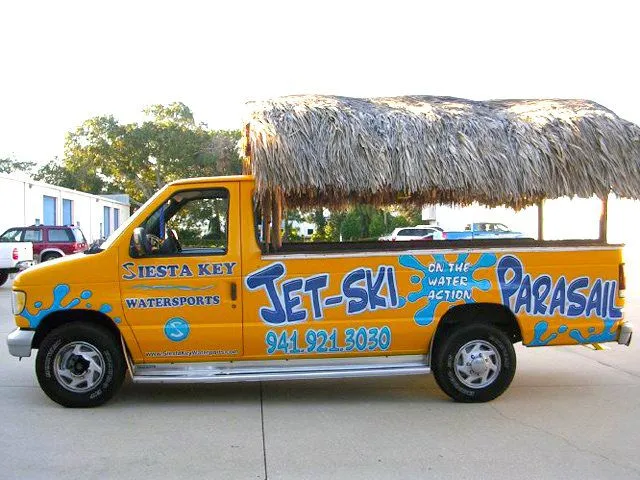 Yellow van with a thatched roof advertising Siesta Key jet-ski and parasailing services, featuring large blue and white text and a contact phone number.