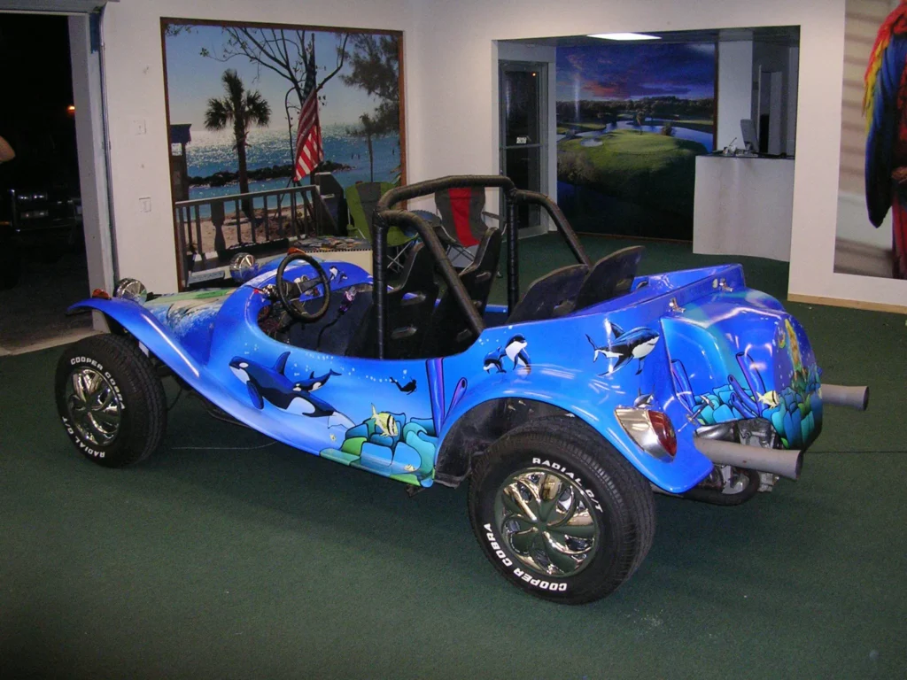 A blue dune buggy with ocean-themed artwork, including orcas and fish, parked indoors on a green carpet.