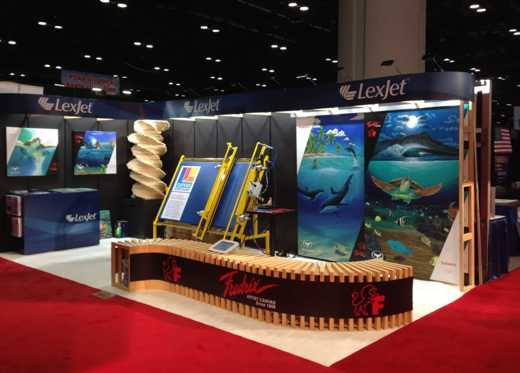 LexJet trade show booth displays large marine-themed prints, promotional banners, literature holders, and a curved wooden counter on a red carpet.
