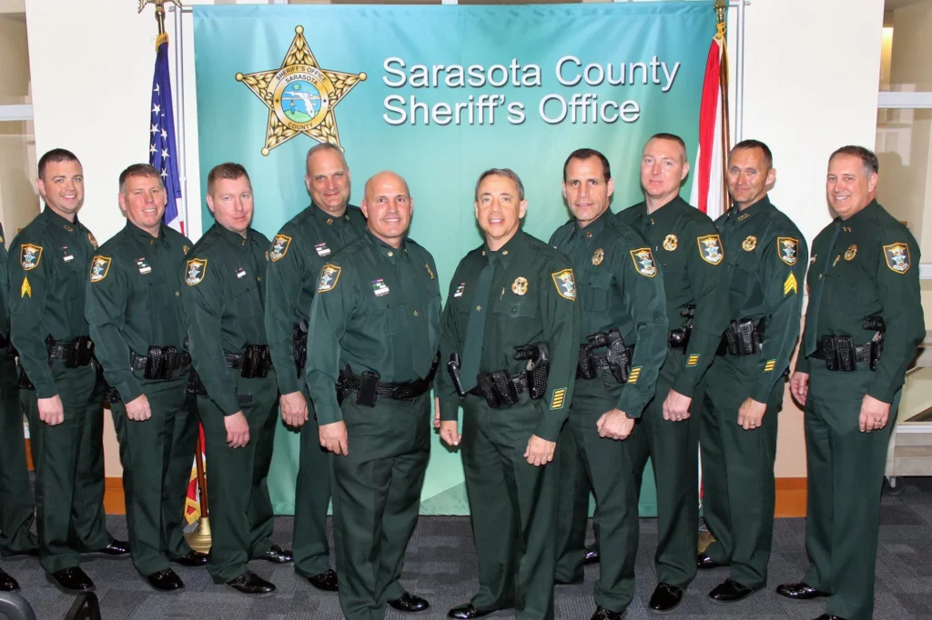 Ten uniformed officers stand in front of a Sarasota County Sheriff’s Office banner, posing for a group photo indoors.