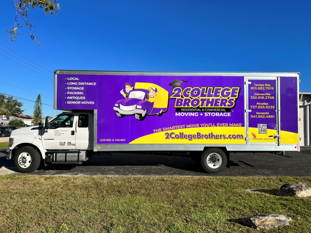 A white moving truck with a large “2 College Brothers” advertisement for moving and storage services, including contact information, on the side panel.