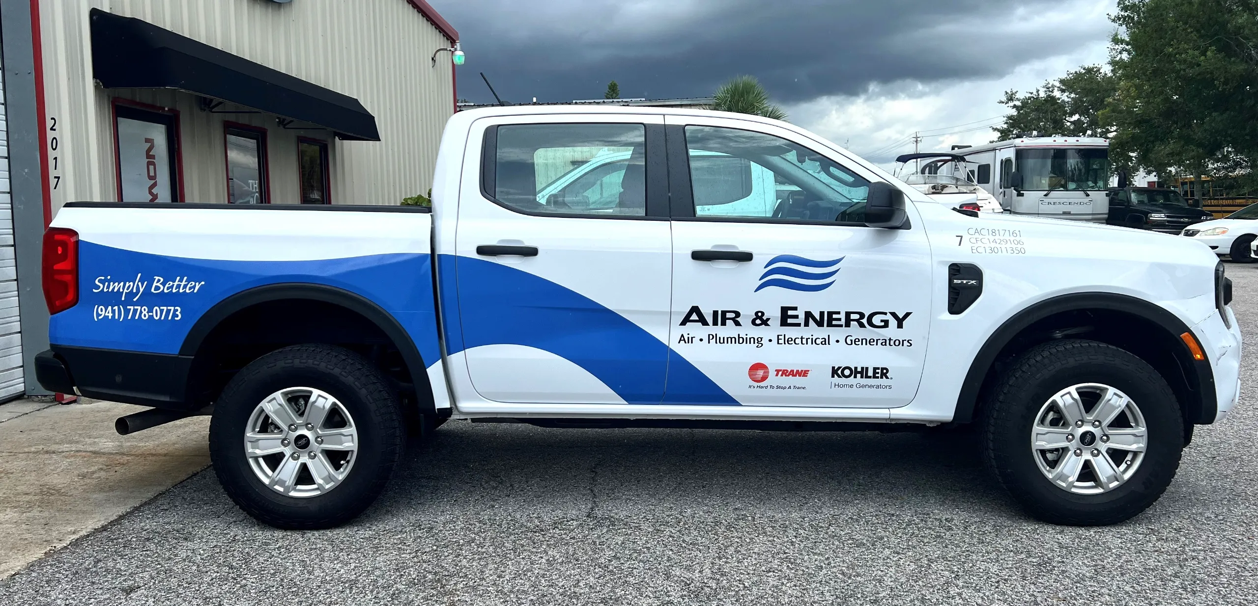 White pickup truck with “Air & Energy” branding and contact information parked outside a building, featuring blue graphics and company service logos on the doors.