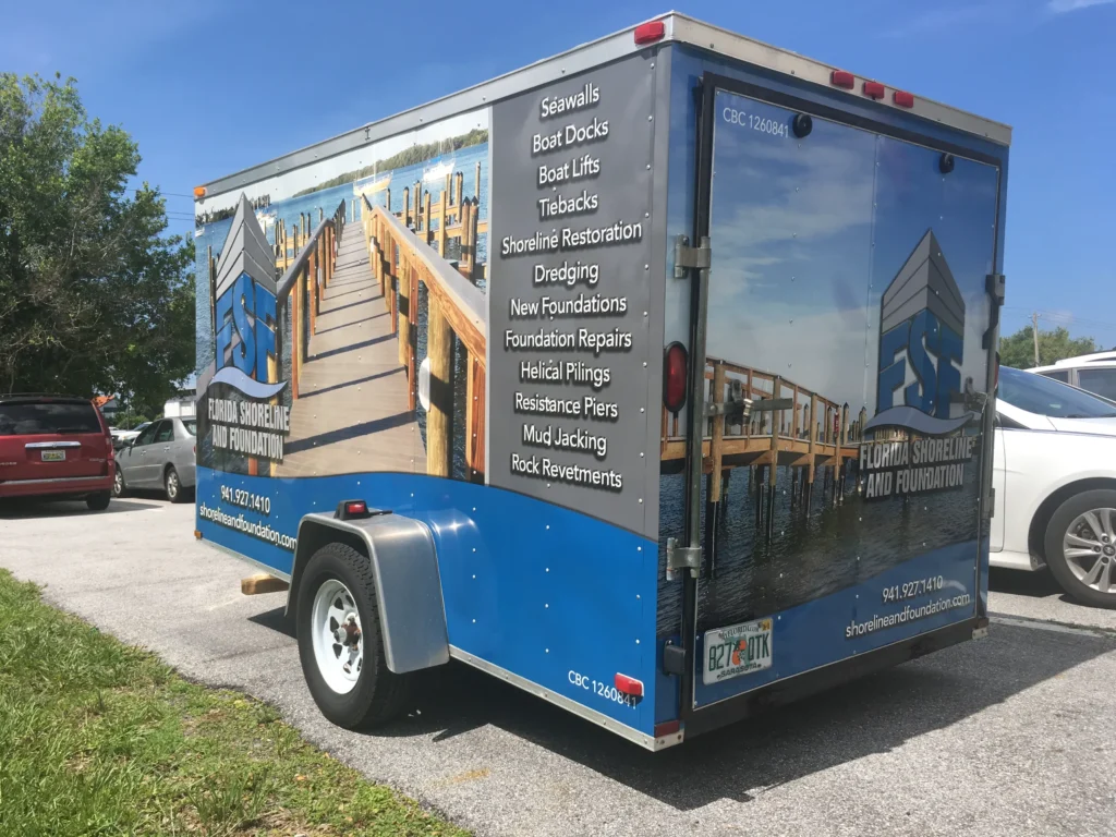 A trailer with Florida Shoreline and Foundations branding, parked in a lot, lists services like seawalls, boat docks, and shoreline restoration on its side.