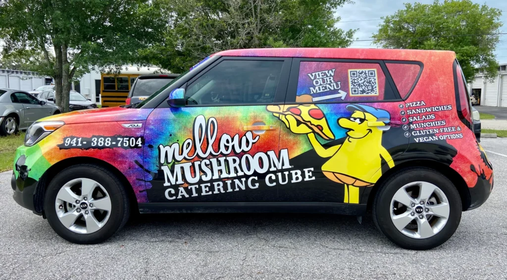 A colorful van with “Mellow Mushroom Catering Cube” branding, cartoon mushroom, menu items listed, a QR code, and contact number parked in a lot.