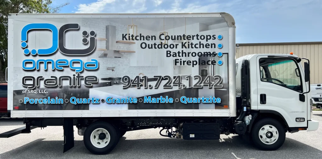 White Omega Granite truck featuring company logo, contact number, and list of services including countertops, outdoor kitchens, bathrooms, fireplace, and materials like quartz, marble, and porcelain.