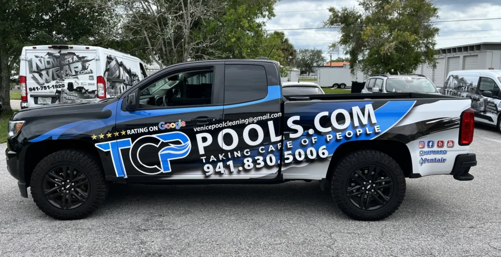 A black and blue TCP Pools pickup truck with company logo, contact info, and social media icons is parked in a lot near other vehicles.