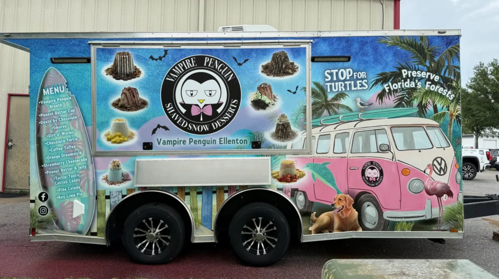 Colorful food truck with “Vampire Penguin Shaved Snow Desserts” branding, a cartoon penguin, dessert images, menu list, and conservation messages for turtles and Florida’s forests.