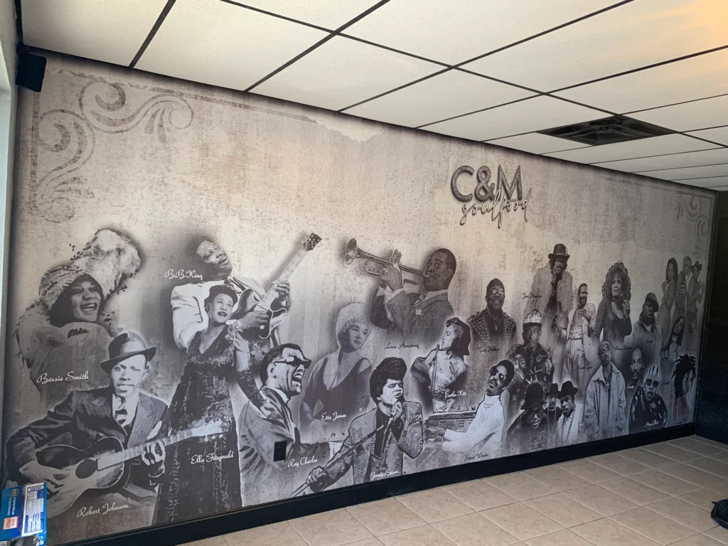 Mural on an interior wall features grayscale portraits of famous jazz and blues musicians with “C&M Soul Food” text at the top.