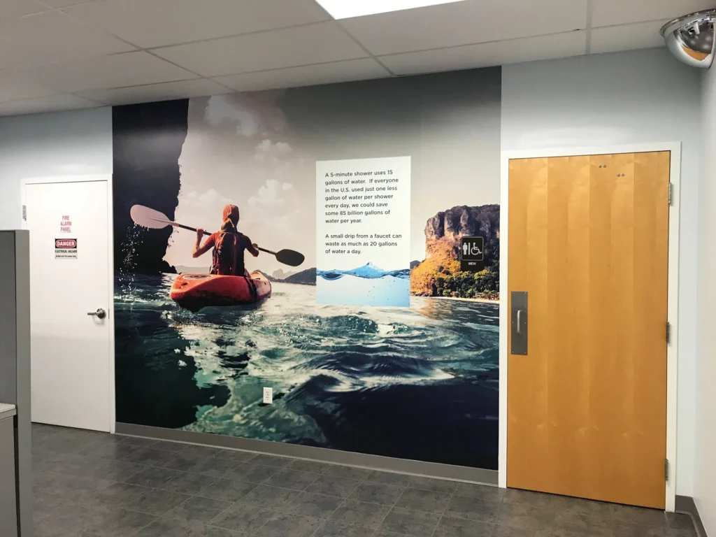 A wall mural of a person kayaking on water, with informational text and a sink graphic, is displayed in a room with gray tile flooring and light-colored doors.